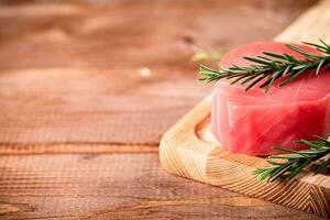 A steak of raw tuna on a cutting board with a sprig of rosemary. photo