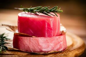 A steak of raw tuna on a cutting board with a sprig of rosemary. photo