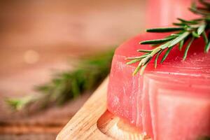 A steak of raw tuna on a cutting board with a sprig of rosemary. photo