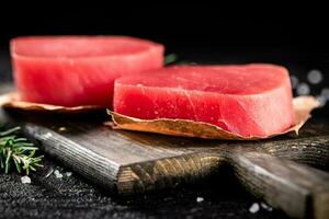 Raw tuna steaks on a rosemary cutting board. photo