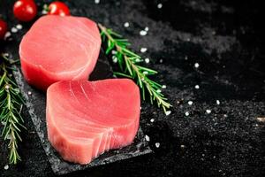 crudo atún en un Roca tablero con Romero y Tomates. foto