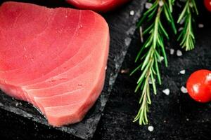 Raw tuna on a stone board with rosemary and tomatoes. photo