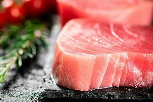 Raw tuna on a stone board with rosemary and tomatoes. photo