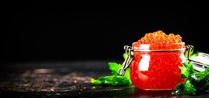 A full jar of red caviar with parsley on the table. photo