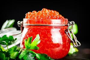 A full jar of red caviar with parsley on the table. photo