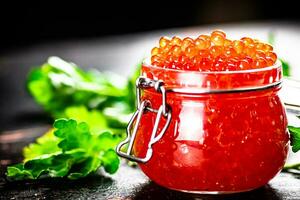 A full jar of red caviar with parsley on the table. photo