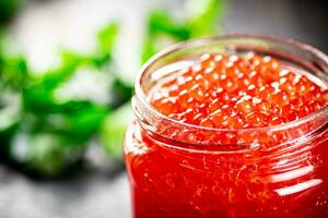 An open jar of red caviar with greens. photo