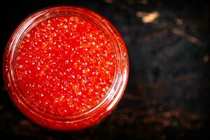 Red caviar in a glass jar. Against a dark background. photo