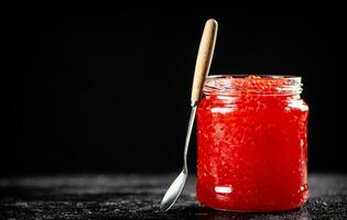 Red caviar in a glass jar on a table with a spoon. photo