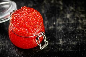 An open glass jar with red caviar on the table. photo