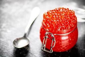 An open glass jar with red caviar on the table. photo