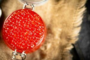 A glass jar with red caviar on burlap. photo