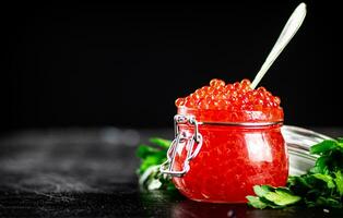 Red caviar in a glass jar with parsley. photo