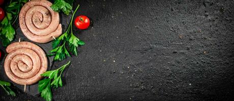 Raw sausages on a stone board with parsley and tomatoes. photo