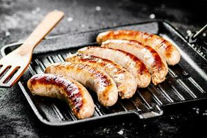 A la parrilla salchichas en un fritura pan con un de madera espátula. foto