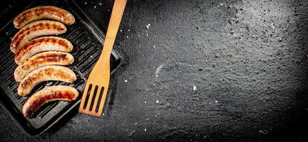 Grilled sausages in a frying pan with a wooden spatula. photo