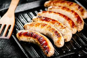 Grilled sausages in a frying pan with a wooden spatula. photo