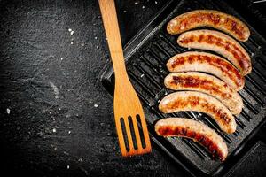 Grilled sausages in a frying pan with a wooden spatula. photo