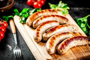 Grilled sausages on a wooden cutting board with parsley and tomatoes. photo