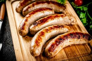 Grilled sausages on a wooden cutting board with parsley and tomatoes. photo