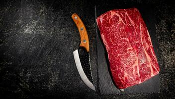 Raw beef on a stone board with a knife. photo