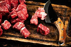 Raw pieces of beef on a cutting board with a knife. photo