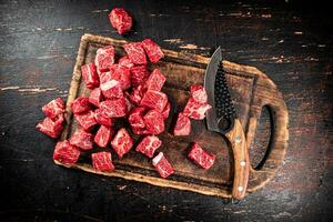 Raw pieces of beef on a cutting board with a knife. photo