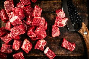 Raw pieces of beef on a cutting board with a knife. photo