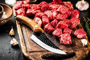 Raw pieces of beef on a cutting board with a knife. photo