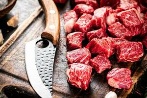 Raw pieces of beef on a cutting board with a knife. photo