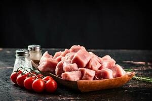 Pieces of raw pork on a wooden plate with spices and tomatoes. photo