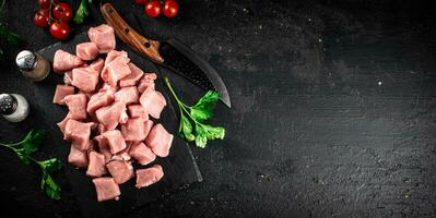 Pieces of raw pork on a stone board with parsley, tomatoes and spices. photo