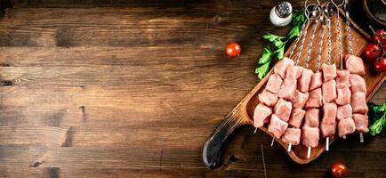 Pork kebab raw on skewers with parsley and tomatoes on a cutting board. photo