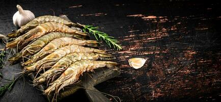 Raw shrimp on a cutting board with rosemary and garlic. photo