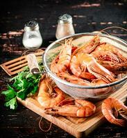 Boiled shrimp in a colander on a cutting board with parsley. photo