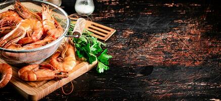 Boiled shrimp in a colander on a cutting board with parsley. photo