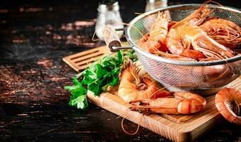 Boiled shrimp in a colander on a cutting board with parsley. photo