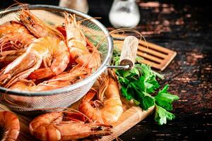 Boiled shrimp in a colander on a cutting board with parsley. photo