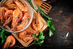 Boiled shrimp in a colander on a cutting board with parsley. photo