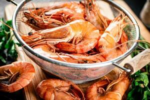 Boiled shrimp in a colander on a cutting board with parsley. photo
