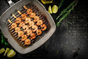 Grilled shrimp on skewers in a frying pan with rosemary and pieces of lime. photo