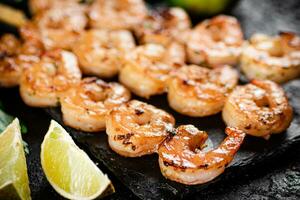 Grilled shrimp on a stone board with pieces of lime. photo