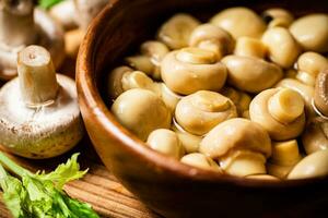 Pickled mushrooms in a bowl on a cutting board with greens. photo