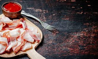 Pieces of bacon on a cutting board with tomato sauce. photo