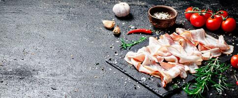 Pieces of bacon on a stone board with tomatoes and rosemary. photo