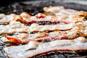 Pieces of bacon are fried in boiling oil with air bubbles. photo