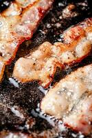 Pieces of bacon are fried in boiling oil with air bubbles. photo