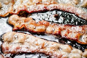 Pieces of bacon are fried in boiling oil with air bubbles. photo