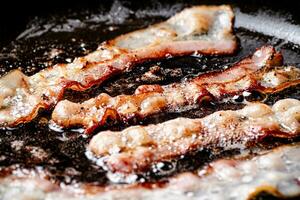 Pieces of bacon are fried in boiling oil with air bubbles. photo