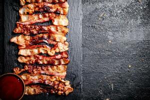 Strips of fried bacon on a stone board with tomato sauce. photo